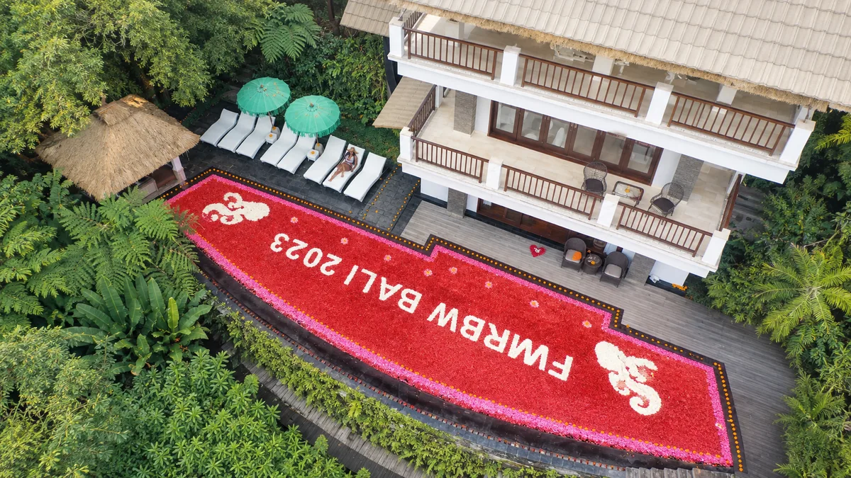 Overhead view of a red floral pool display with white lettering beside a two-story building and sun loungers