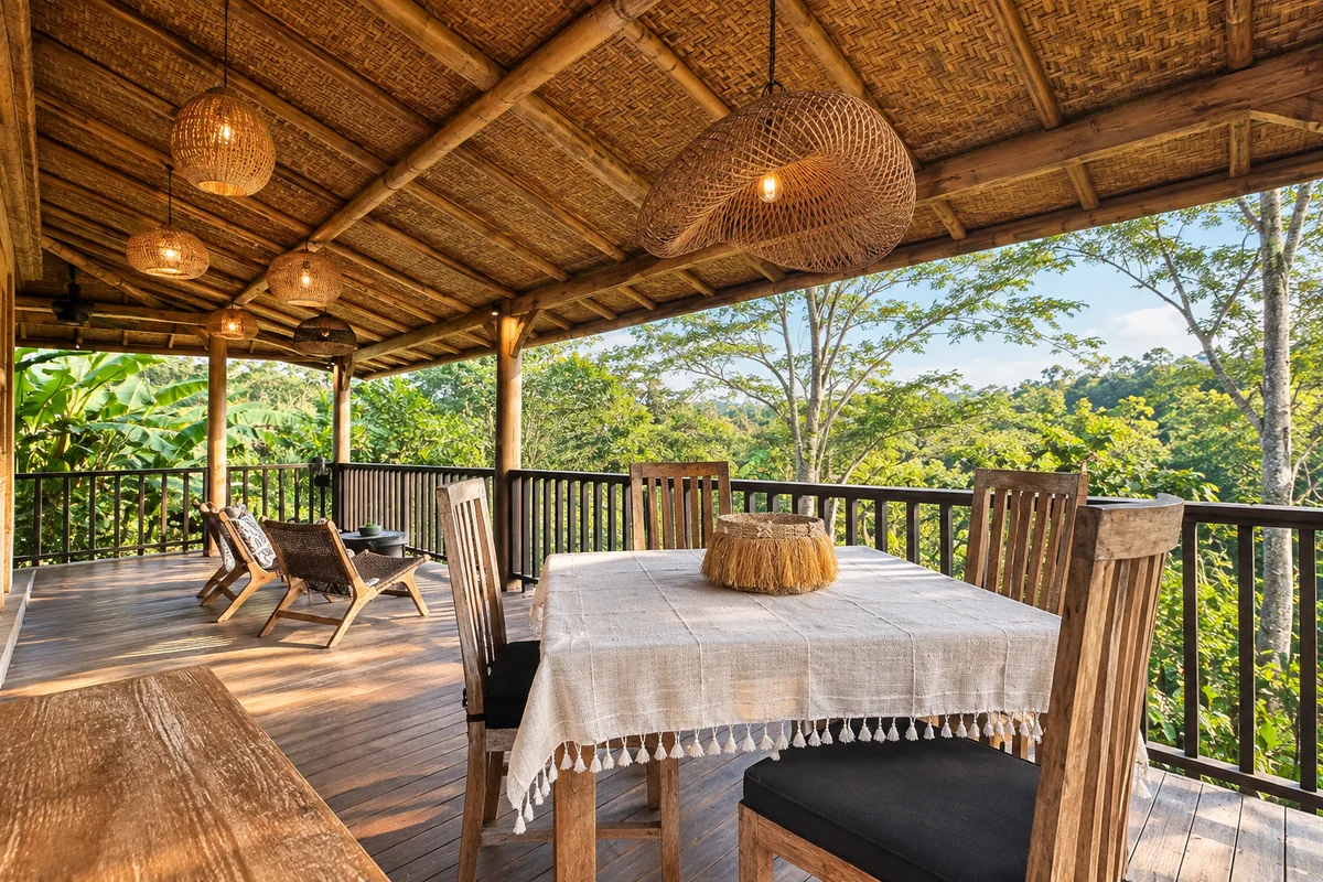 White-clothed table and woven chairs on a covered timber balcony overlooking tropical trees