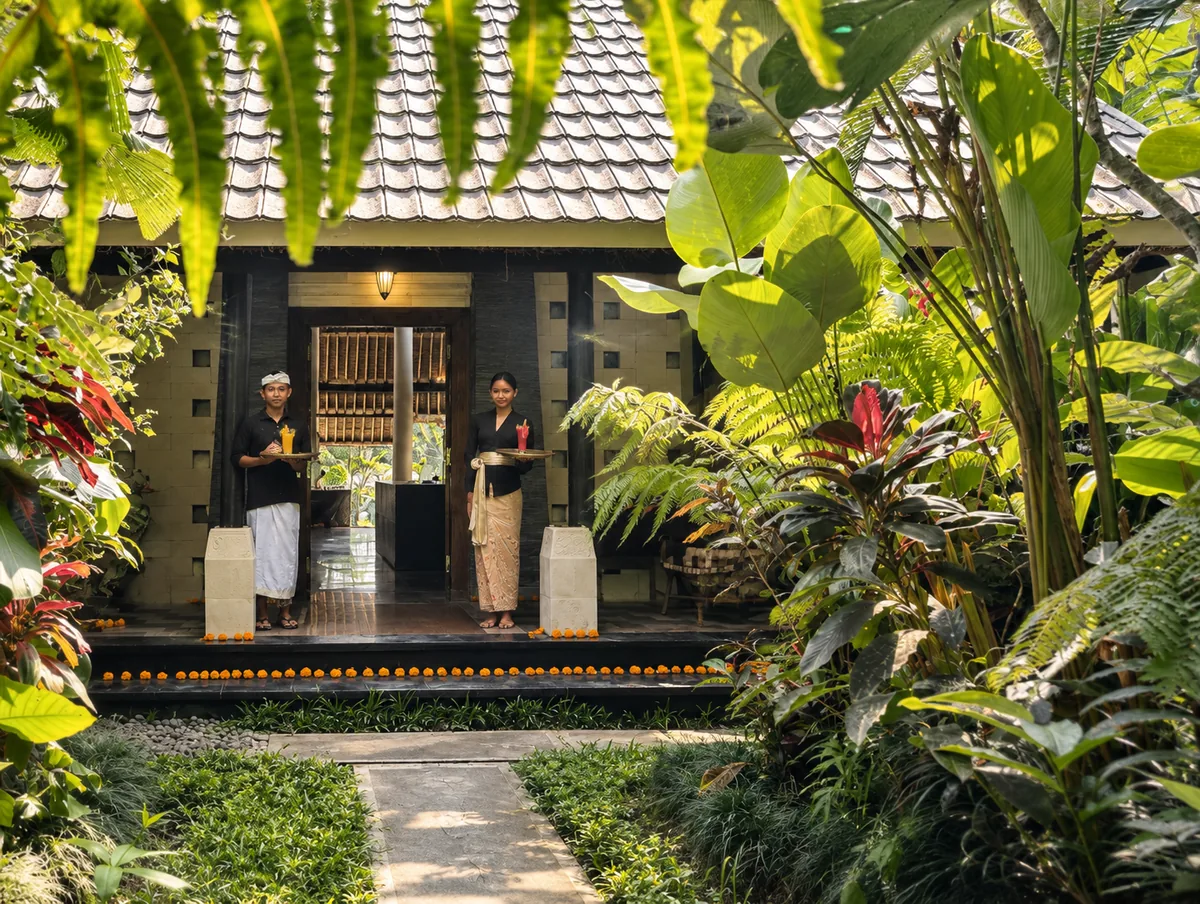 Two people standing at a timber entrance framed by ferns, palms and a garden path