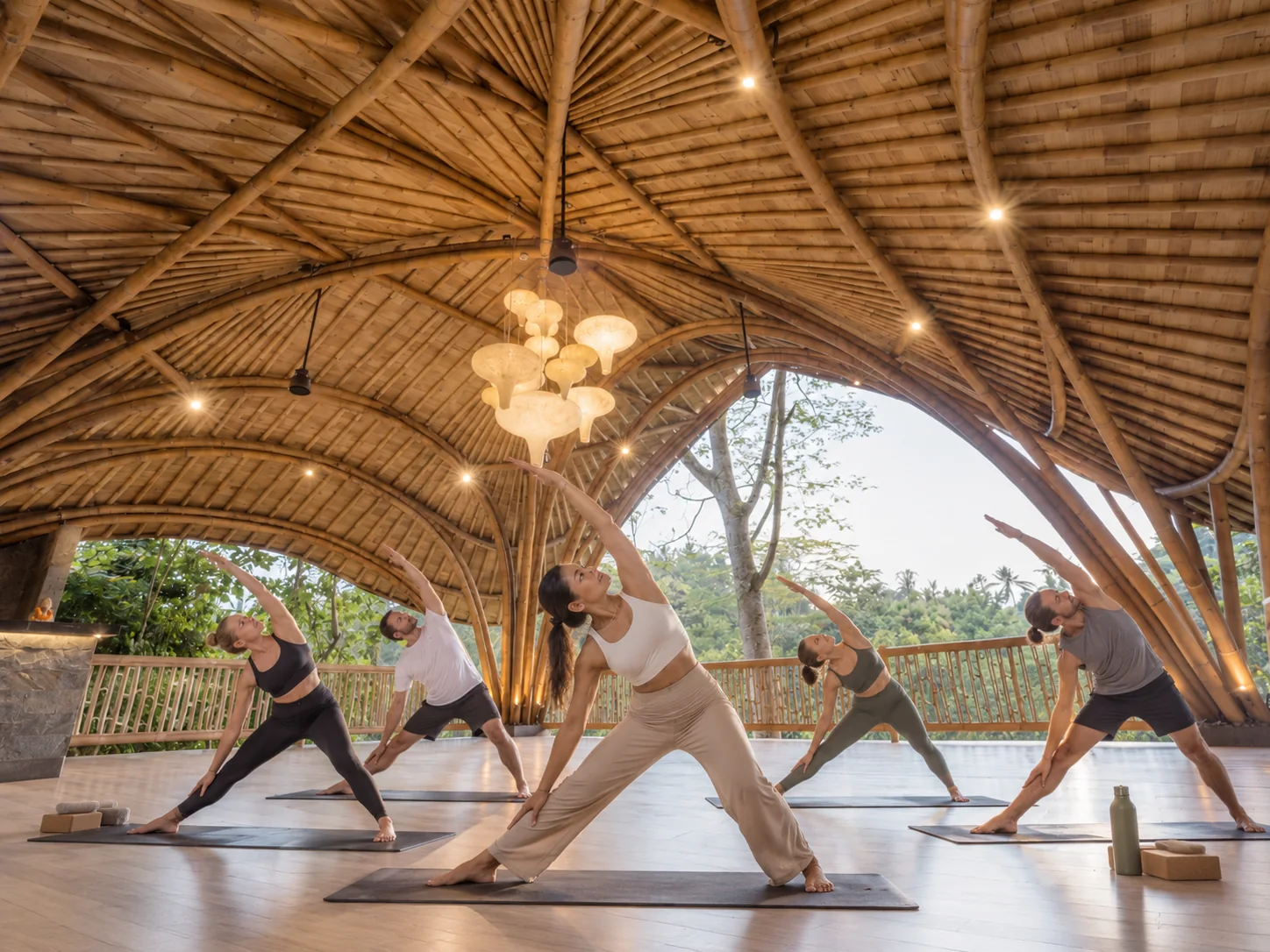 Group practicing yoga beneath an open bamboo pavilion overlooking tropical greenery