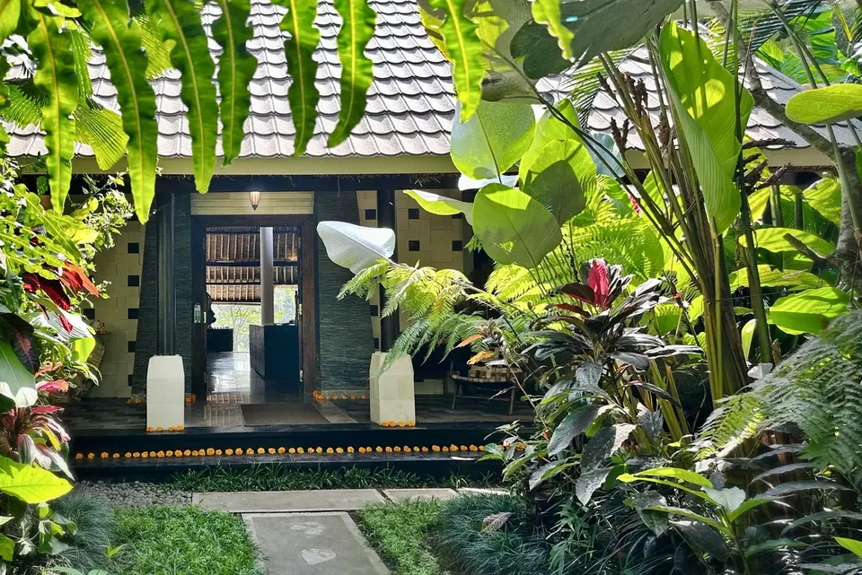 Tropical foliage framing the timber doorway and stone path at The Manipura Estate