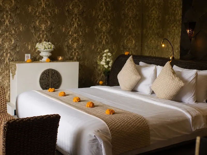 Large double bed in Golden Room with white linen, woven cushions and gold-patterned wallpaper