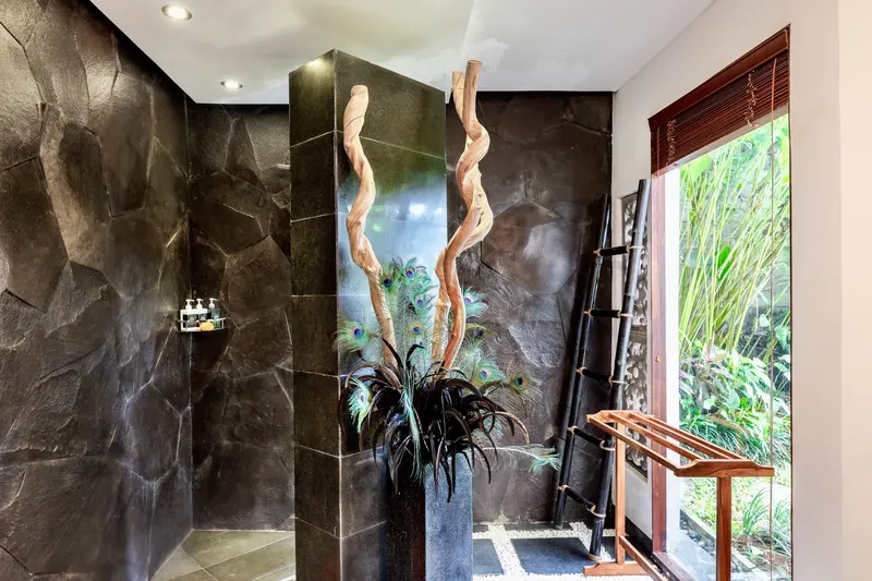 Stone-lined shower area in Golden Room beside a window overlooking tropical plants