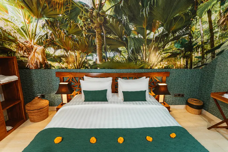 Green Room 1 double bed beneath a large tropical palm mural with green accents and timber bedside lamps