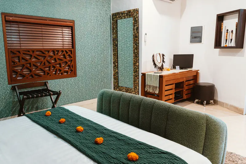 View across the Green Room 1 bed towards teal textured walls, carved timber window panel, full-length mirror and desk