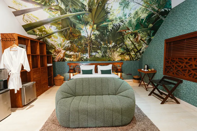 Wide view of Green Room 1 with a tropical wall mural, double bed, curved green bench, storage and timber furniture
