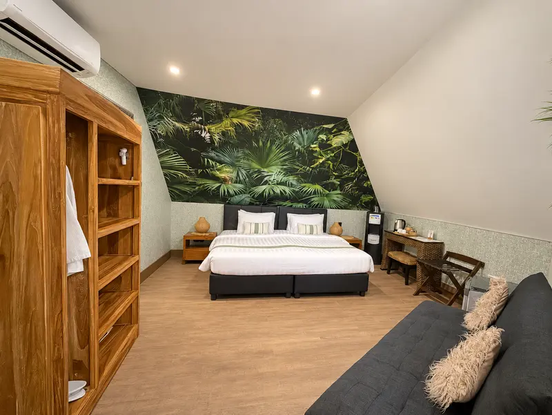 Green Room 2 bedroom with a large double bed, tropical palm mural, timber storage, writing desk and dark sofa