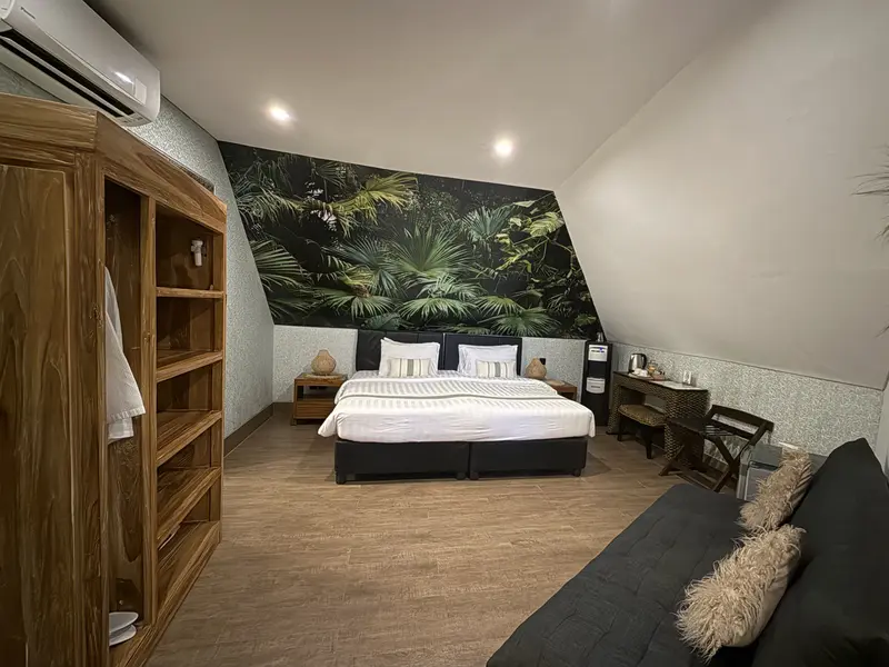 Full view of Green Room 2 with bed, sofa, timber wardrobe, writing desk and tropical feature wall