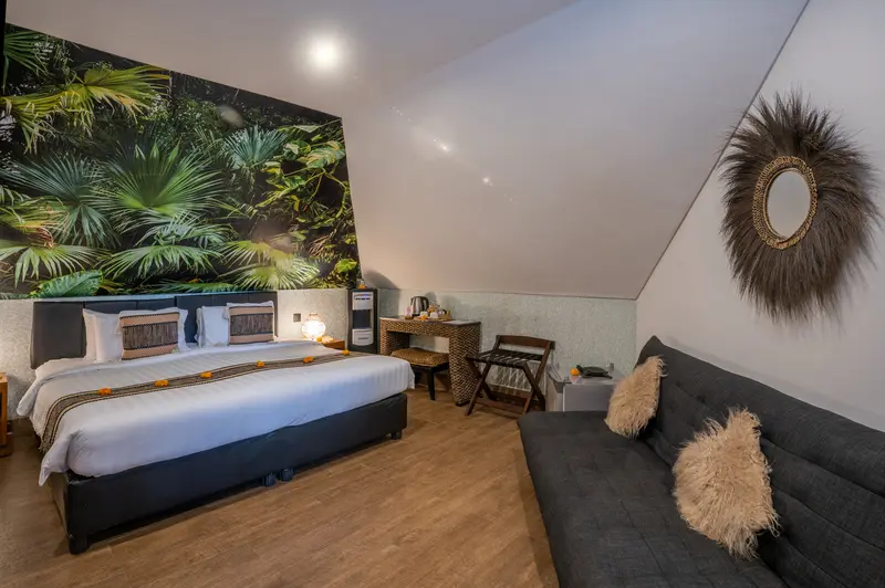Wide view of Green Room 2 with a large double bed, botanical wall mural, writing desk and dark upholstered sofa