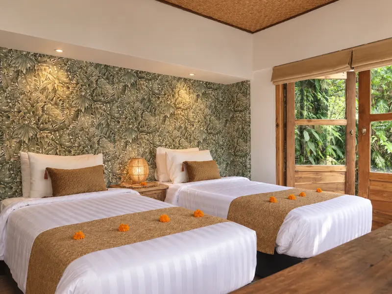 Front view of two single beds in Joglo 1st Floor against a deep green botanical wall