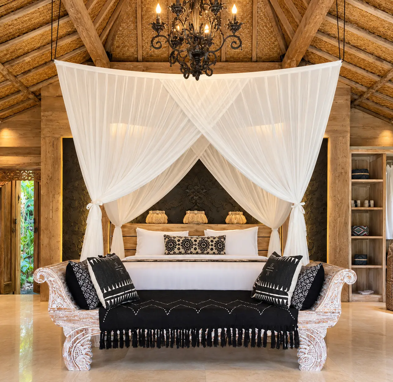 Main Joglo Room with a tall timber roof, chandelier, draped bed and carved dark wooden furniture
