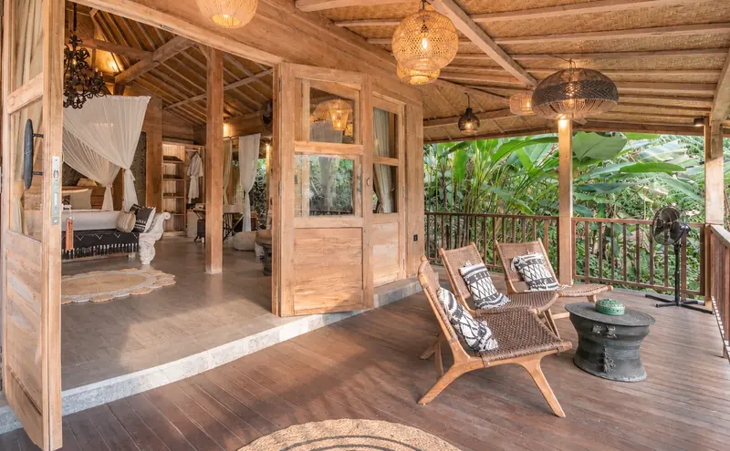 Covered timber balcony outside Main Joglo Room with woven chairs and dense tropical greenery