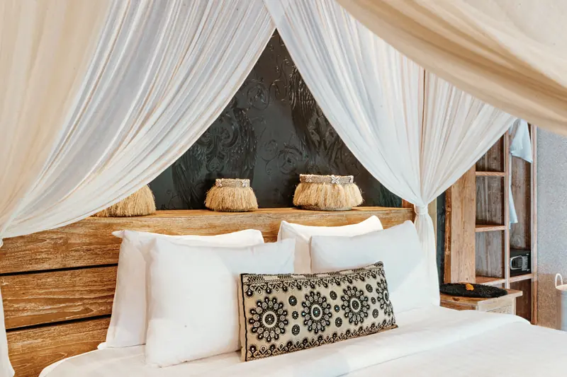 Close view of the Main Joglo Room canopy bed with crisp white linen, woven cushions and carved timber