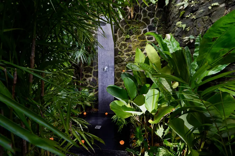 Separate outdoor garden shower for Main Joglo Room surrounded by tropical planting and a dark stone wall