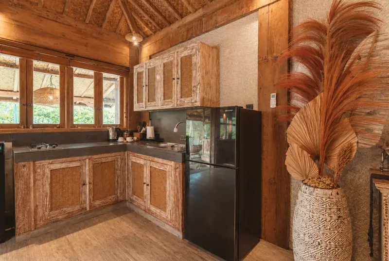 Main Joglo Room kitchenette with carved timber cabinets, sink, two-burner hob, refrigerator and kettle