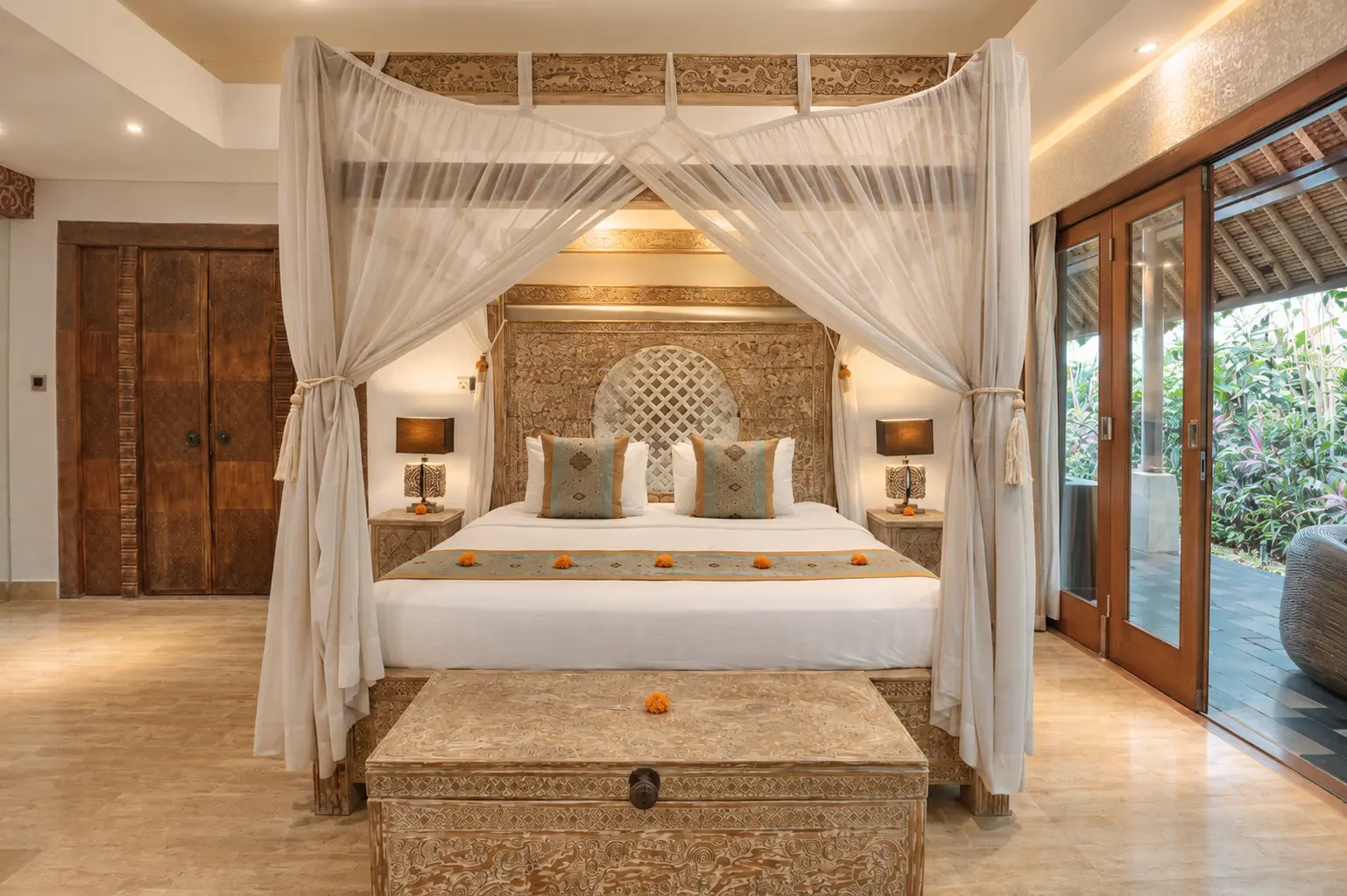 Red Room with a canopy bed, carved wooden bench and tall glazed doors beside tropical greenery