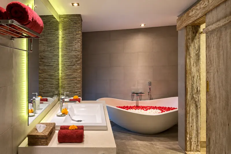 Freestanding bathtub filled with red and white petals beside the illuminated Red Room vanity