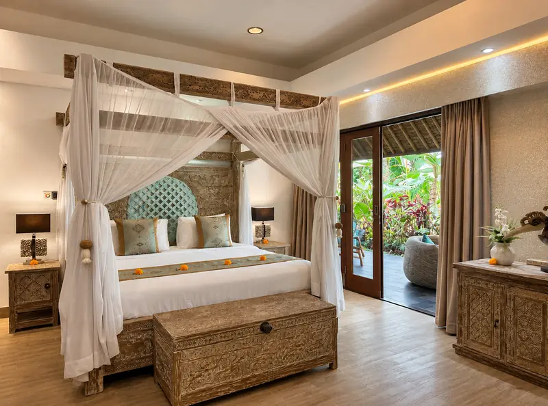 Red Room canopy bed beside tall timber-framed glass doors opening towards tropical plants