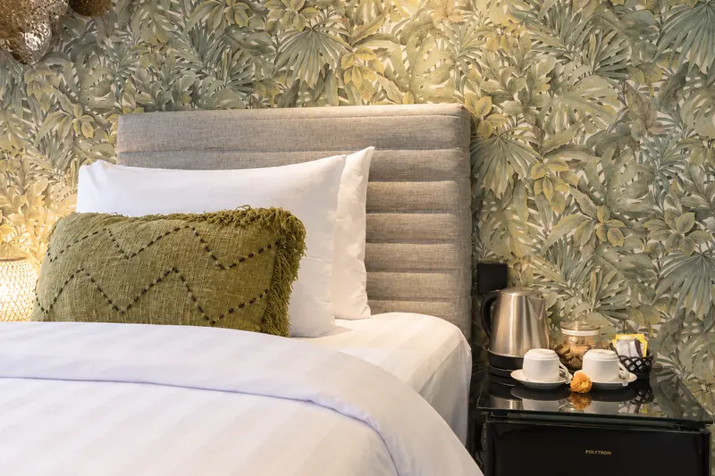 Close view of a River Villa Room 1 single bed, botanical wall covering, woven cushion, kettle and cups