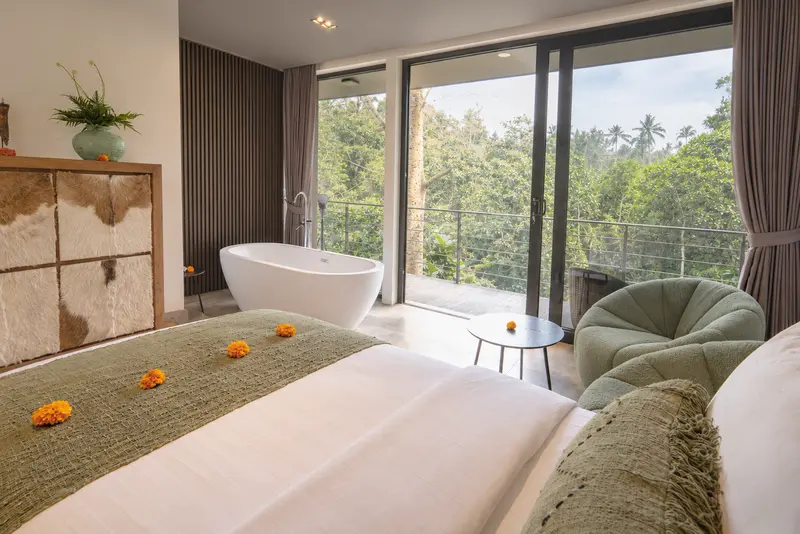 View from the twin beds across River Villa Room 1 towards the freestanding bathtub, lounge chair and tropical outlook