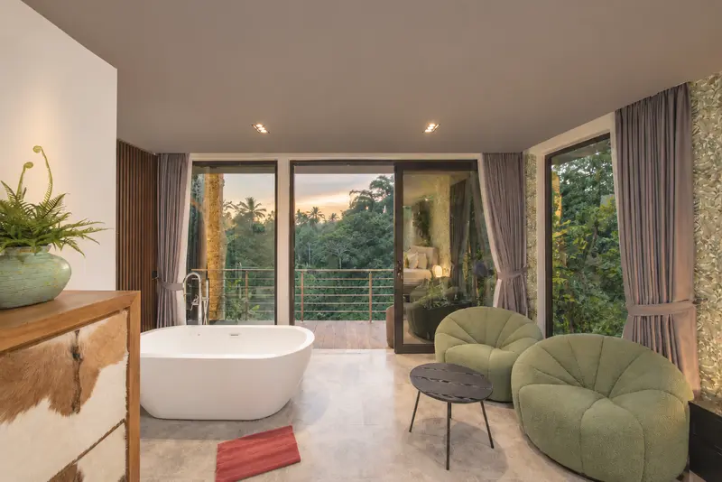 River Villa Room 1 lounge area with two green chairs, round table, storage cabinet and freestanding bathtub