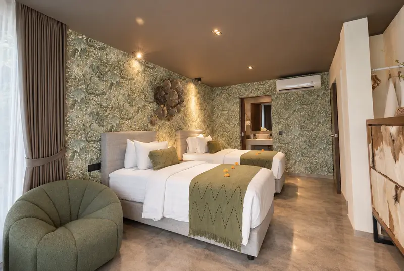 Side view of River Villa Room 1 with twin beds, botanical walls, lounge chair, cabinet and air conditioning