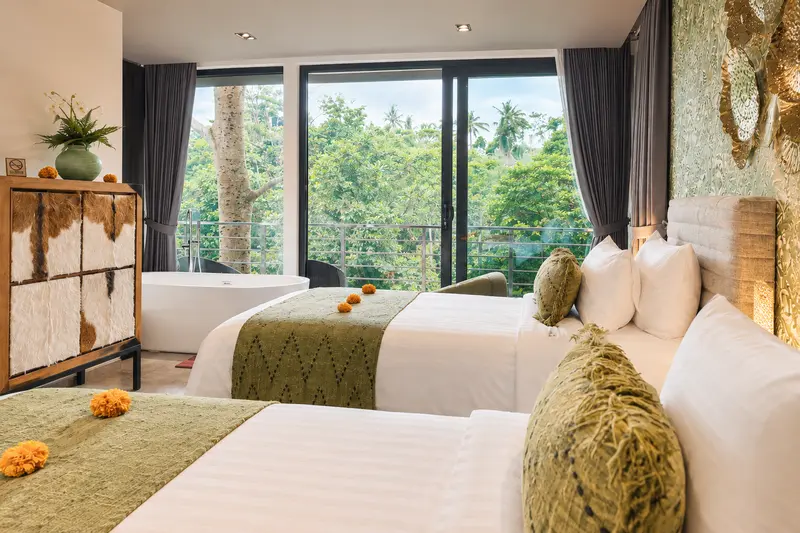 Wide diagonal view across River Villa Room 1 showing twin beds, cabinet, freestanding bath and glass doors
