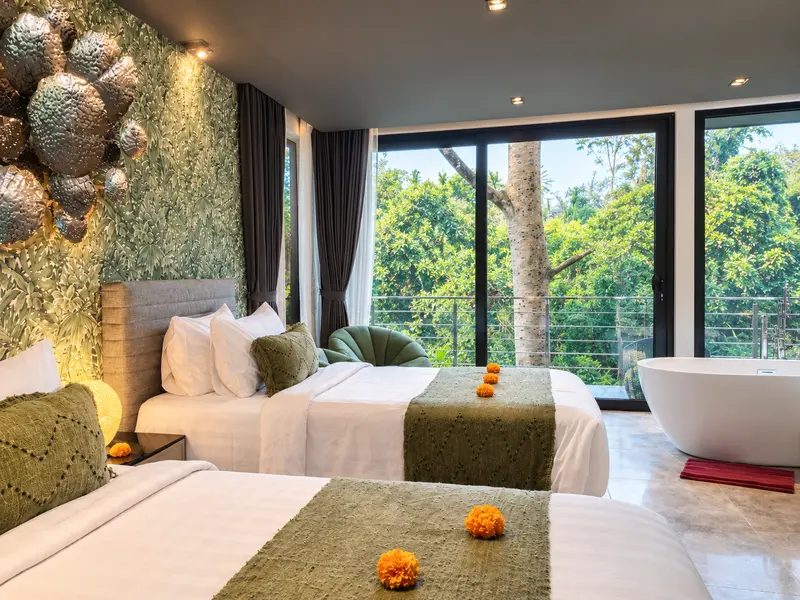 River Villa Room 2 twin beds beside the freestanding bathtub and glazed doors looking into tropical greenery