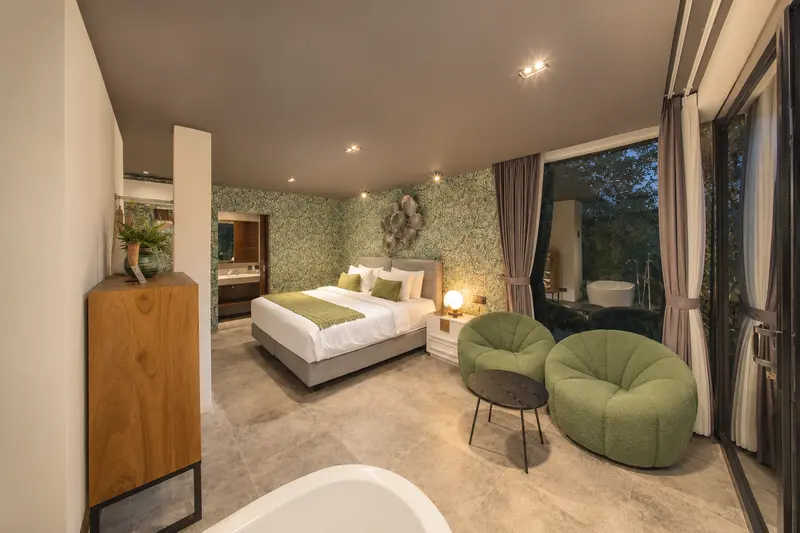 Wide view of River Villa Room 2 with twin beds, lounge chairs, bathtub and full-height glass doors