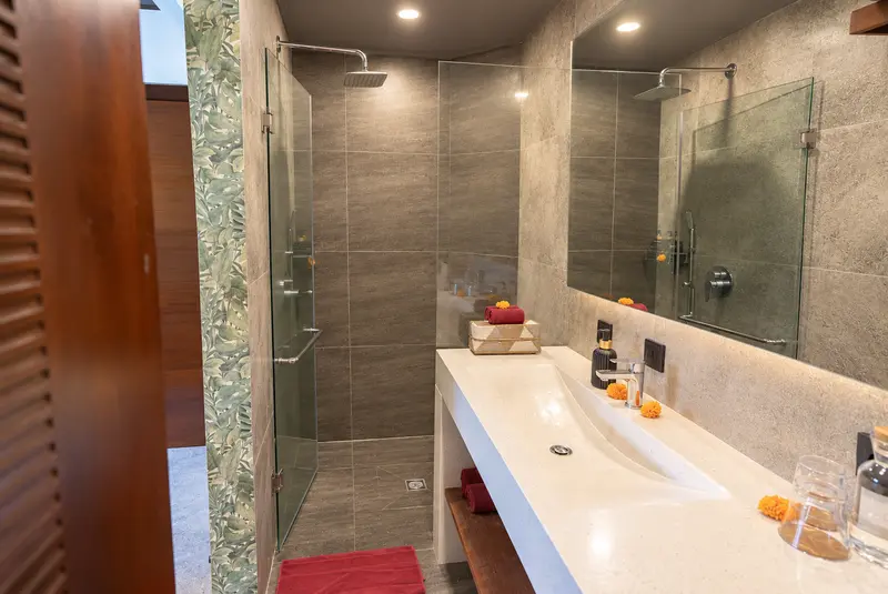 River Villa Room 2 bathroom with a long washbasin, wide mirror and glass-enclosed rain shower