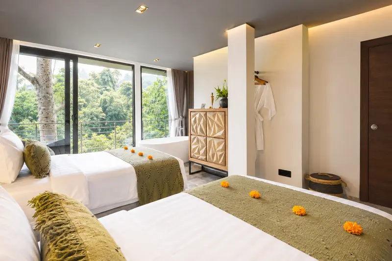 View across the two single beds in River Villa Room 2 towards wide glass doors and tropical trees