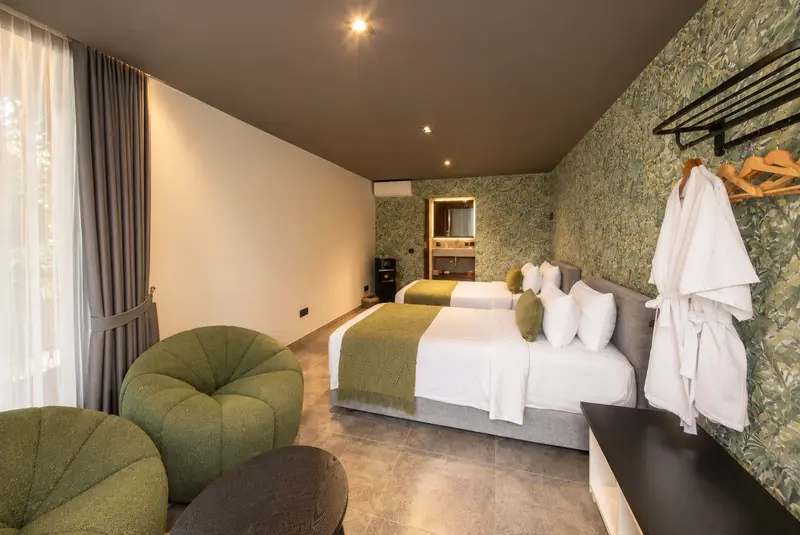 Reverse view of River Villa Room 3 showing twin beds, two green lounge chairs, small table and hanging space