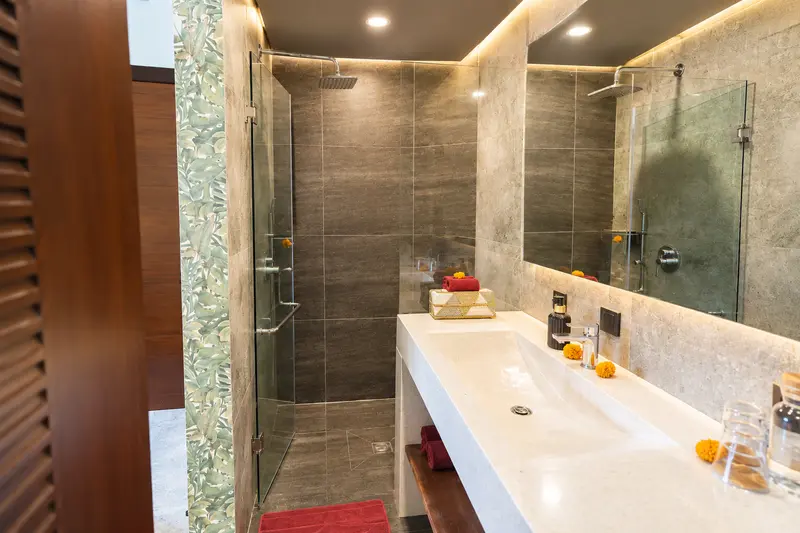 River Villa Room 3 bathroom viewed through a timber door with glass shower, washbasin and botanical wall edge