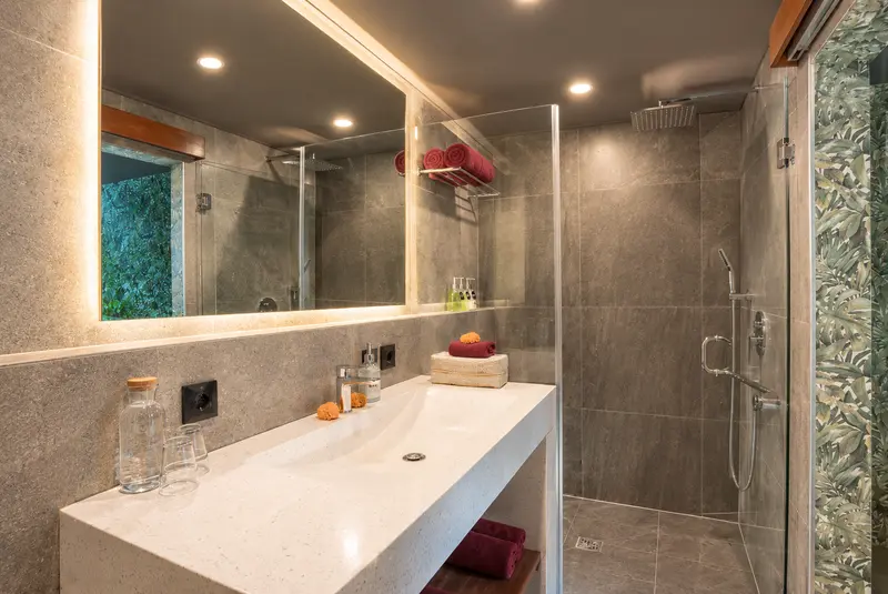 River Villa Room 3 bathroom with a long washbasin, wide mirror and glass-enclosed rain shower