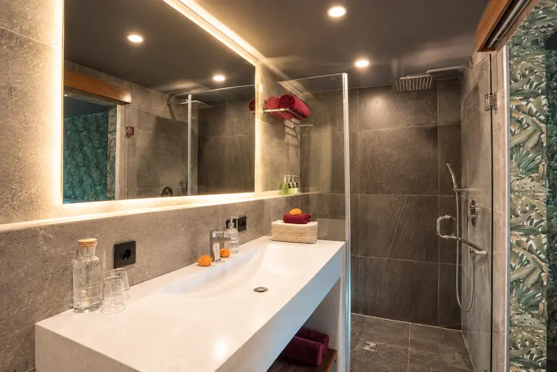 River Villa Room 4 bathroom with a long washbasin, illuminated mirror and glass-enclosed rain shower