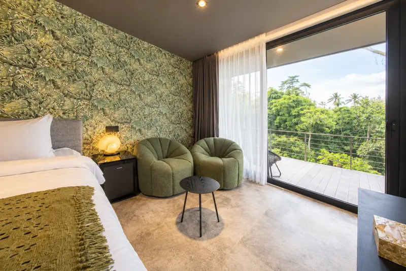 Two green lounge chairs beside full-height glazing and the tropical-view terrace of River Villa Room 4
