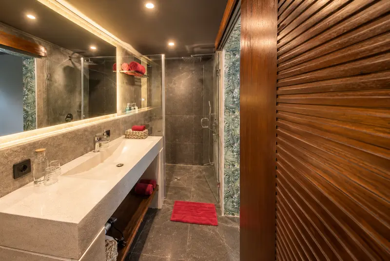 River Villa Room 5 bathroom with a long washbasin, illuminated mirror and glass-enclosed rain shower