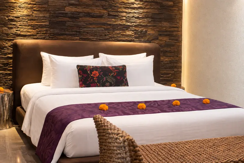 Closer view of the Studio Room 1 bed with plum runner, floral cushion and layered dark-stone wall