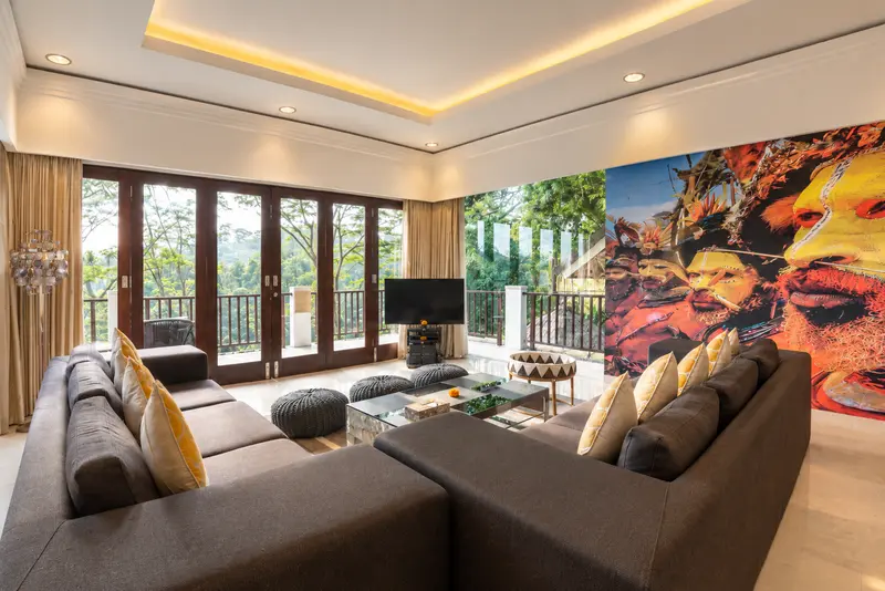 Reverse view of Studio Room 1 lounge with sectional sofas, media screen, vivid artwork and garden-facing doors