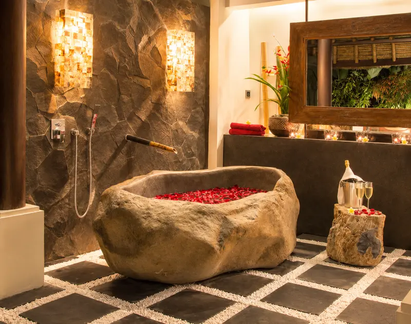 Sculptural freestanding stone bathtub in Studio Room 1 with stone wall, warm lighting and garden reflections