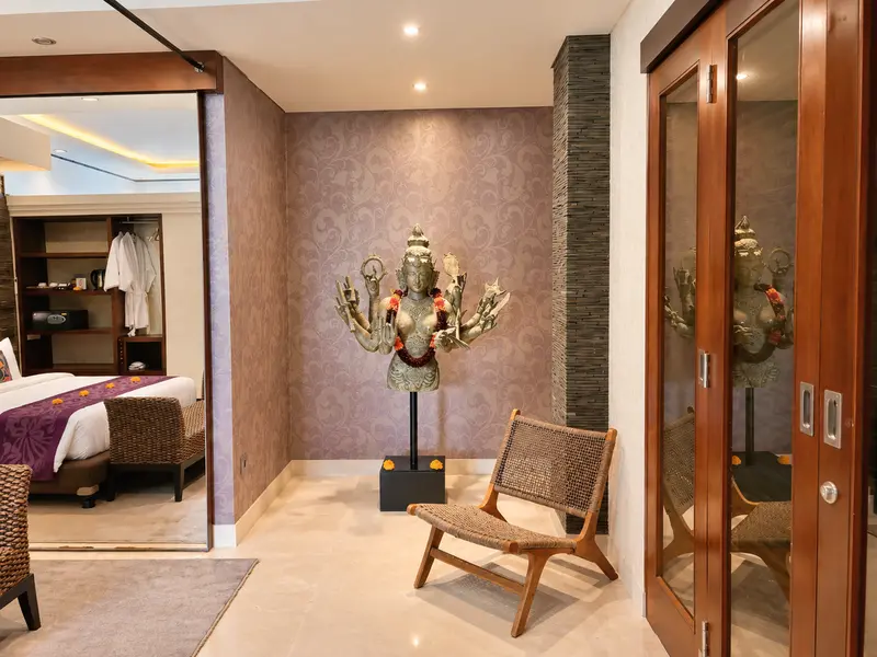 Studio Room 1 transition space with sculptural artwork, lounge chair, timber doors and a view back to the bed