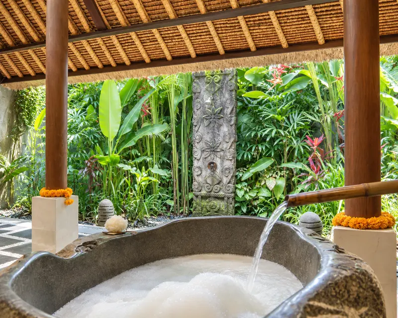 Sculptural stone bathtub in Studio Room 2 beneath a timber roof and facing dense tropical planting