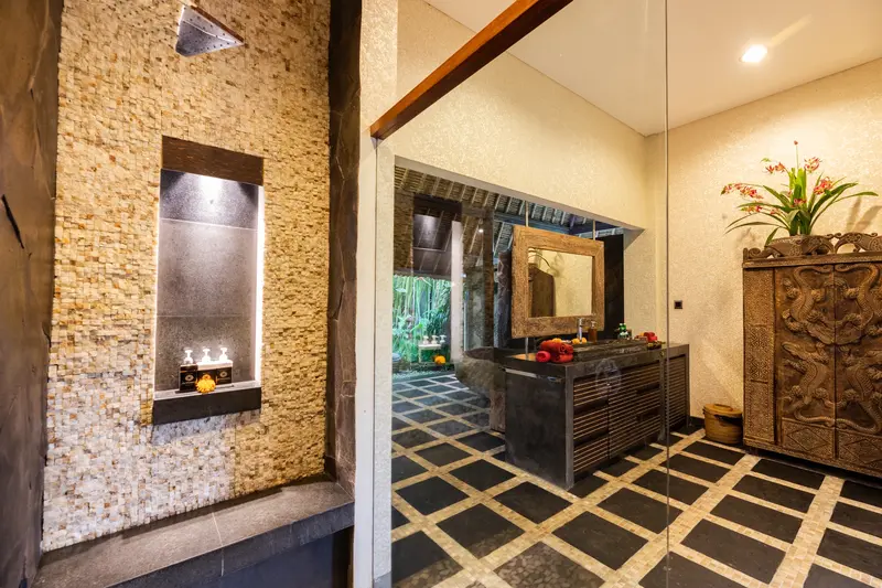 Studio Room 2 glass-enclosed walk-in shower with square rain head, textured stone walls and pebble floor