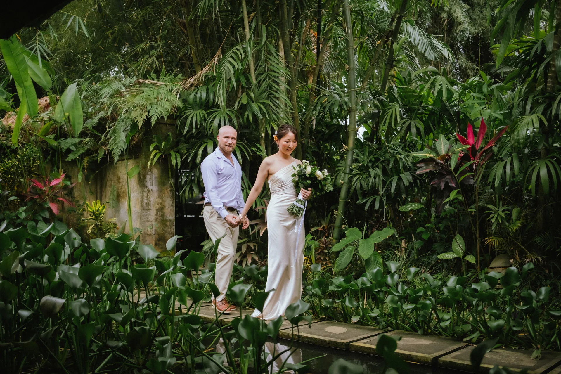 Couple holding hands on a garden path surrounded by tropical foliage
