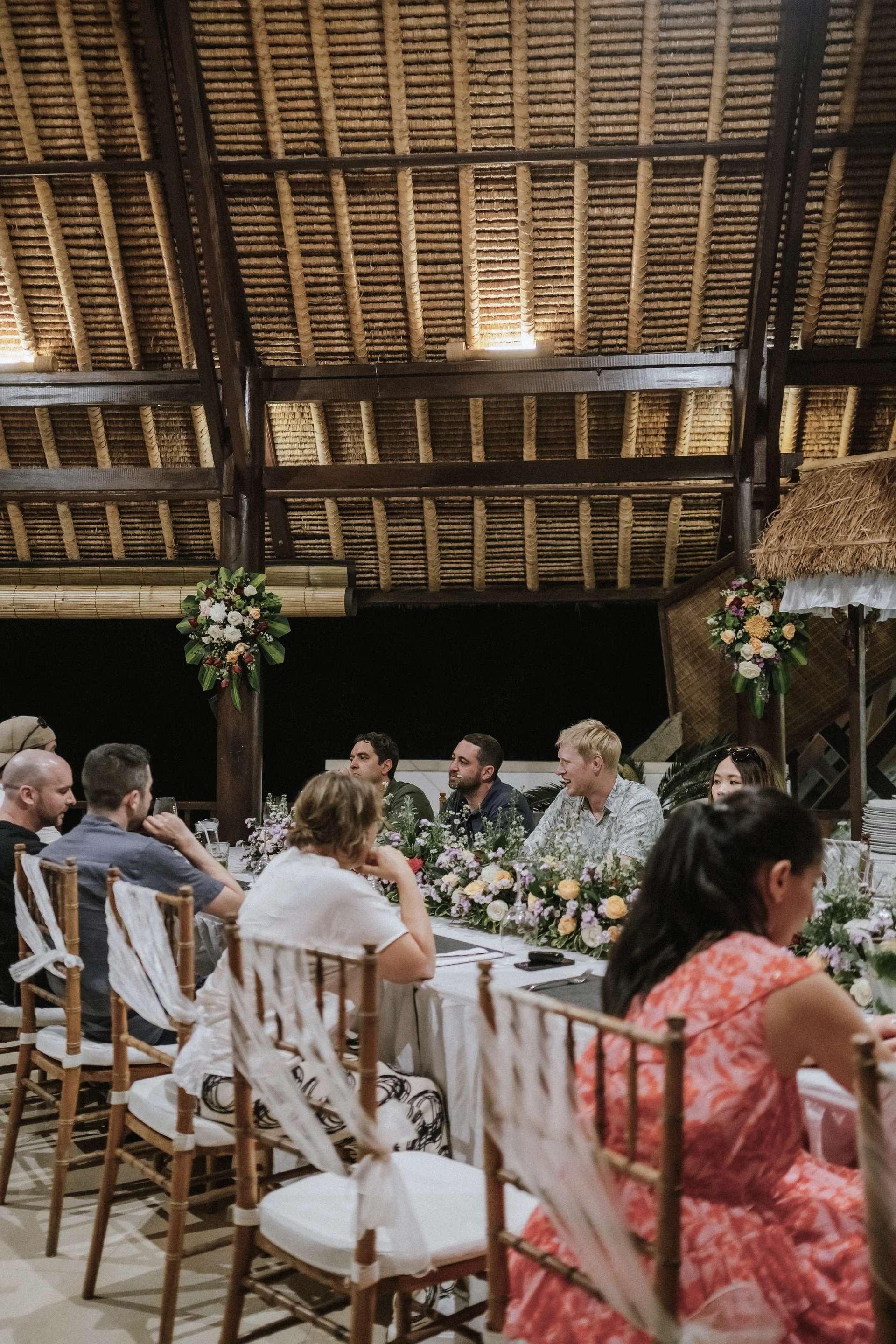 Guests sharing a meal at a long reception table beneath a timber roof